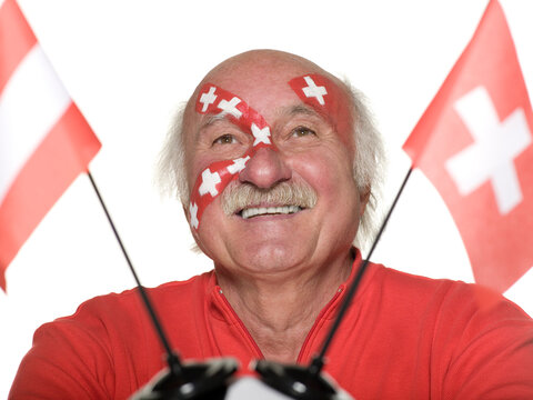 Senior man with Swiss flag painted on face holding football, Austrian and Swiss flag aside