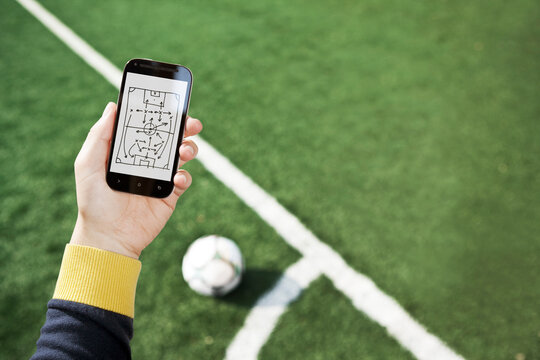 Hand holding smart phone with match tactics over soccer field