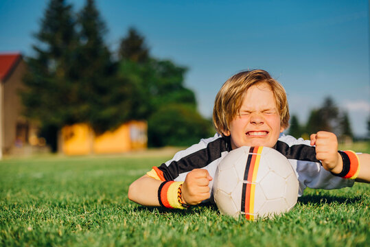 Boy in German soccer shirt lying on grass, keeping fingers crossed for world championship