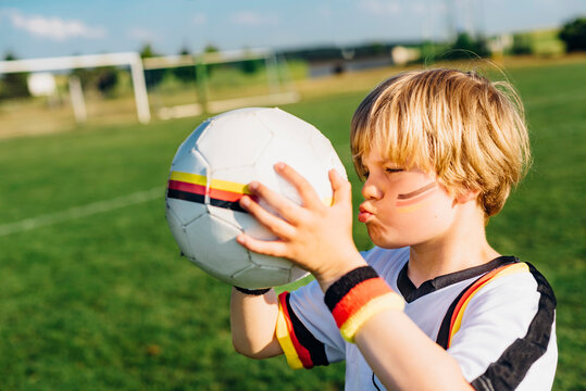 Boy with face paint and German football shirt, kissing soccer ball