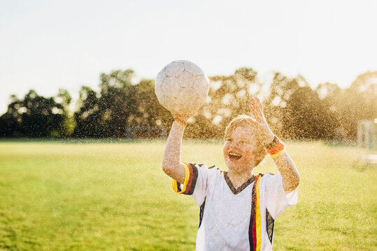 Boy wearing German soccer shirt screaming for joy, standing in water splashes