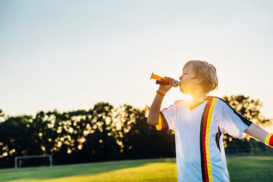 Boy wearing German soccer shirt, blowing horns on soccer field