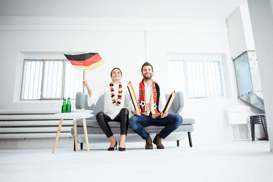 Happy German football fan couple sitting on couch watching Tv