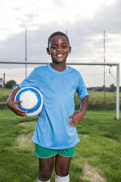 Portrait of smiling young football player holding ball on football ground