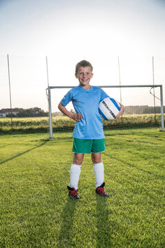 Portrait of smiling young football player holding ball on football ground