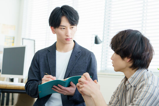 カウンセリング　話を聞きながらメモをとる若い日本人カウンセラー