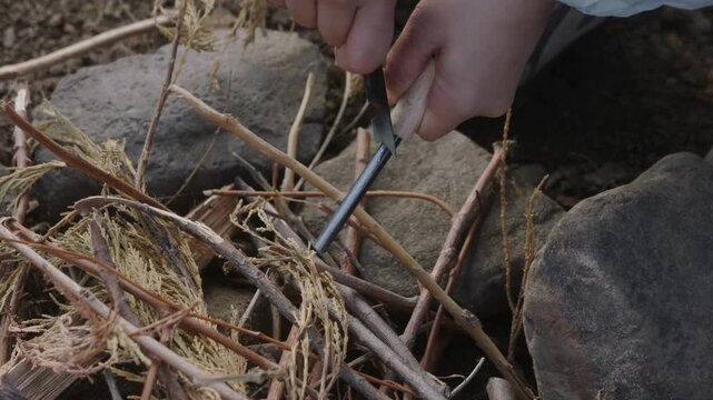 Close-up of hands striking a ferro rod to create sparks for starting a campfire in the wilderness