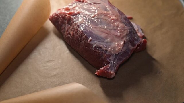 A person unwraps a package containing a raw meat cut on a clean surface.