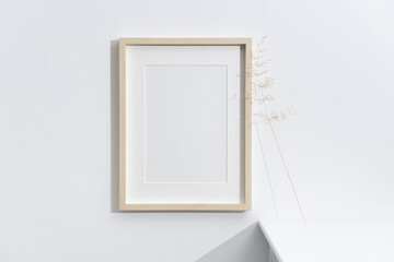 Blank vertical photo frame on white wall with a delicate dried grass stem, styled in a clean, minimal and modern white interior © nikavera