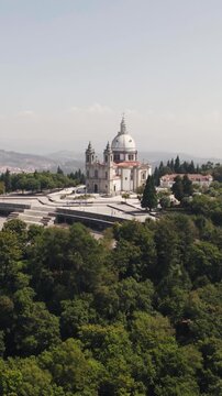 Vertical aerial view of the hilltop Sameiro Sanctuary surrounded by lush forest in Braga, Portugal.