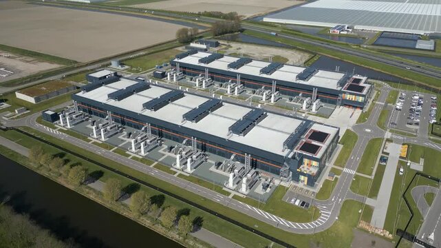 Ultra wide aerial view of a massive European hyperscale data center surrounded by farmland and wind turbines.