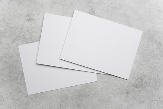 Three blank white sheets of paper arranged on a textured gray concrete surface, ideal for mockups or design projects requiring copy space
