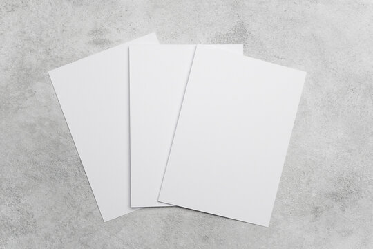 Three blank white sheets of paper arranged on a textured gray surface, ideal for design mockups or presentations