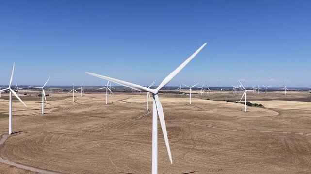 Aerial view of a large wind farm with rotating turbines generating clean, alternative power against a clear blue sky, highlighting sustainable electricity production in a rural landscape