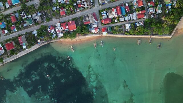 Aerial top-down shot of Magnesia Del Norte in Virac, Catanduanes with shoreline homes, clear water, and coastal road - Philippines