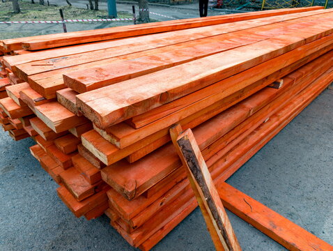 Stacks of wooden planks coated with a protective anti-mold treatment, arranged neatly outdoors on a concrete surface, showcasing the vibrant orange finish applied to preserve the wood quality and prev