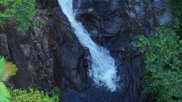 Drone pull-up reveal of the beautiful Sauzier waterfall cascading into a dark pool, surrounded by lush tropical rainforest and palm trees in Port Glaud, Mahe, Seychelles. 30fps 006
