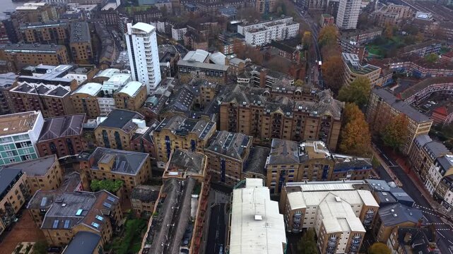 The Shad Wick neighborhood of Southwark London in autumn showing dense apartment complexes, vibrant trees with fall colors, and urban architecture at daytime - sweeping, tilt down, aerial flyover