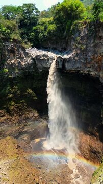 Spectacular drone flyover of Kapas Biru waterfall Java &ndash; Amazing tropical rainforest valley with misty morning fog and majestic red cliff walls, premium Indonesia tourism advertising background