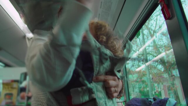 Mother standing inside bus securing toddler in front carrier while traveling evoking multitasking care responsibility balance and focused everyday parenting in urban transit