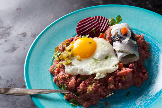 Plate of Labskaus with potatoes, rollmops, pickled gherkin, beetroot and fried egg
