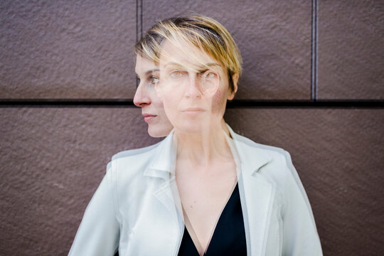 Blond businesswoman leaning against wall, dopple exposure