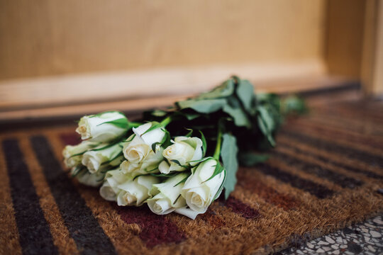 Bunch of white farewell flowers lying on floor mat at apartment door of deceased neighbour