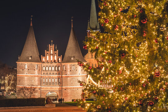 Germany, Schleswig-Holstein, Lubeck, Illuminated Holstentor gate at night with glowing Christmas tree in foreground