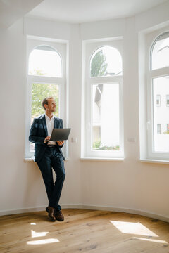 Estate agent waiting in newly refurbished home, holding laptop