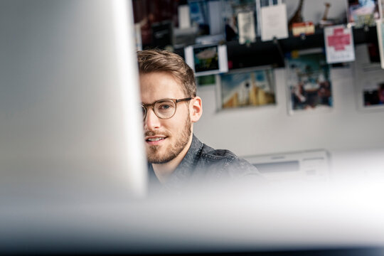 Portrait of young man behind computer screen at desk at home