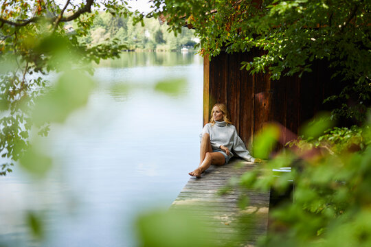 Relaxed woman sitting on wooden jetty at a remote lake