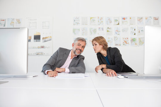 Two whispering colleagues at their desks in an office