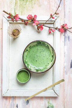Matcha tea in bowl, with match powder, spoon and chasen and pink flowers