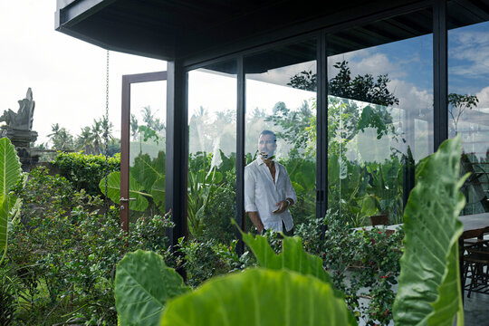 Mature man standing in his modern house, looking through window