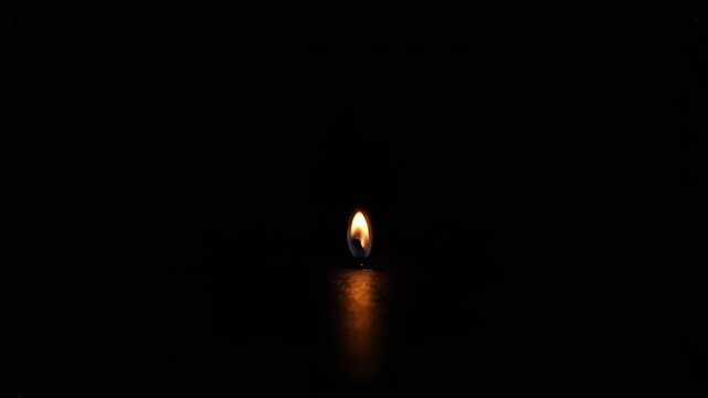Close up of a small bright flame flickering on a dark surface before suddenly getting blown out