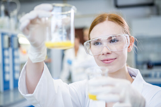 Scientist in lab holding up two beakers with liquid