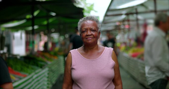 African American elderly woman standing at outdoor market looking at camera with calm serious expression conveying dignity strength presence and lived experience