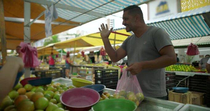 Hispanic street vendor placing citrus fruit into plastic bag for customer at outdoor market expressing routine service trust and everyday local food commerce