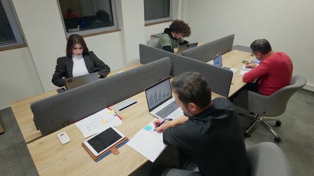 Colleagues are focused on their tasks, utilizing laptops and tablets in a contemporary office environment. Professionals diligently perform their duties within a bright and organized workspace.
