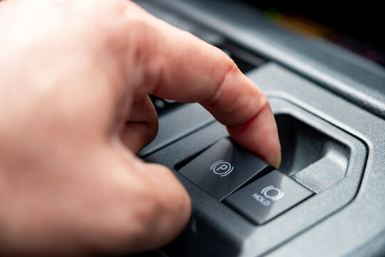 Close up of a driver pulling electronic parking brake switch on a car console panel. Modern automatic handbrake and auto hold safety system concept for commercial automotive vehicle interior