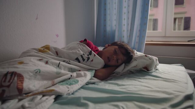 Young boy sleeping on side in bed with blanket partially covering face showing vulnerability comfort and peaceful childhood rest