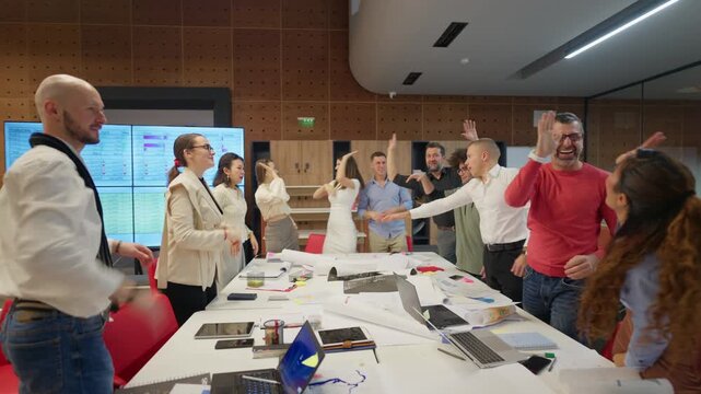 Diverse coworkers joyfully celebrate a successful project completion with high fives and enthusiastic cheers in a modern office.
