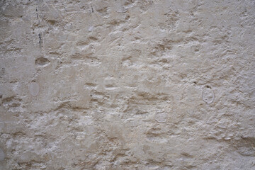 Fototapeta premium Rough beige stone wall background with pits and weathered architectural texture