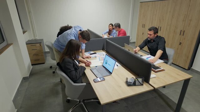 Businesspeople actively engage in collaborative work within a bright, contemporary office setting. Employees effectively utilize technology while performing their daily tasks and discussions.
