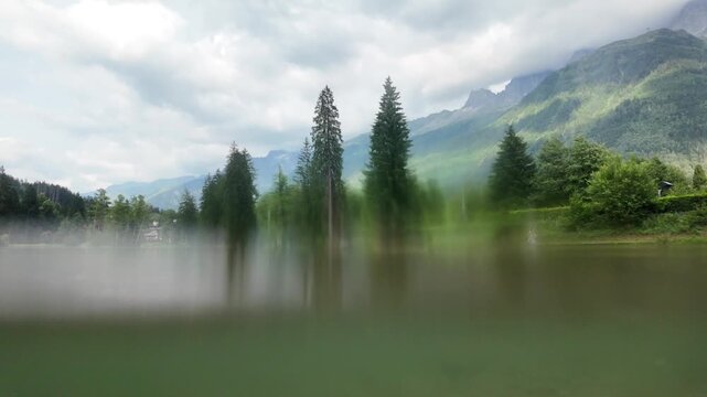 Split shot of an alpine lake, with a view of the chamonix mountains and the lush forest, and a view of the murky underwater world on a cloudy summer day in france