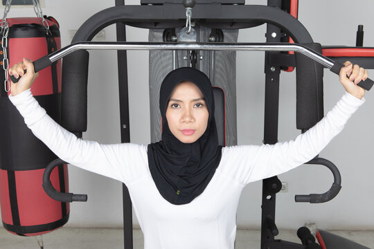 Focused Asian Muslim woman wearing black hijab exercising on chest press machine at the gym