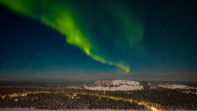 Aerial view of the vibrant green Aurora Borealis dancing over the snow-covered fells and pine forests of Luosto at night in Sodankyla, Lapland, Finland.