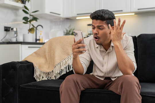 Indian man at home plays mobile game loses round makes facepalm upset yet ready for rematch. Arabian guy on sofa taps try again on smartphone plans comeback focuses on next level and score recovery