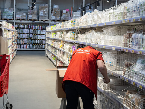 Kyiv, Ukraine - March 20, 2026: Auchan employee restocking shelves with disposable tableware in a retail store, showing daily warehouse operations and inventory management workflow
