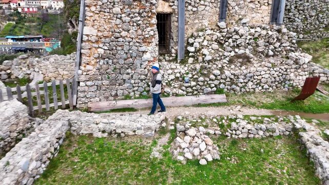 Aerial perspective pulling away and rising from DIY Destinations host Charles Huang to reveal the historic stone walls of Kruje Castle and the surrounding Albanian landscape